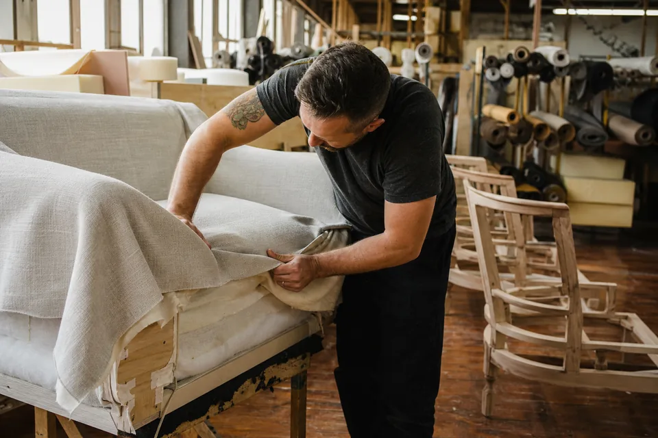 Upholsterer fitting fabric over a sofa frame in a US furniture workshop